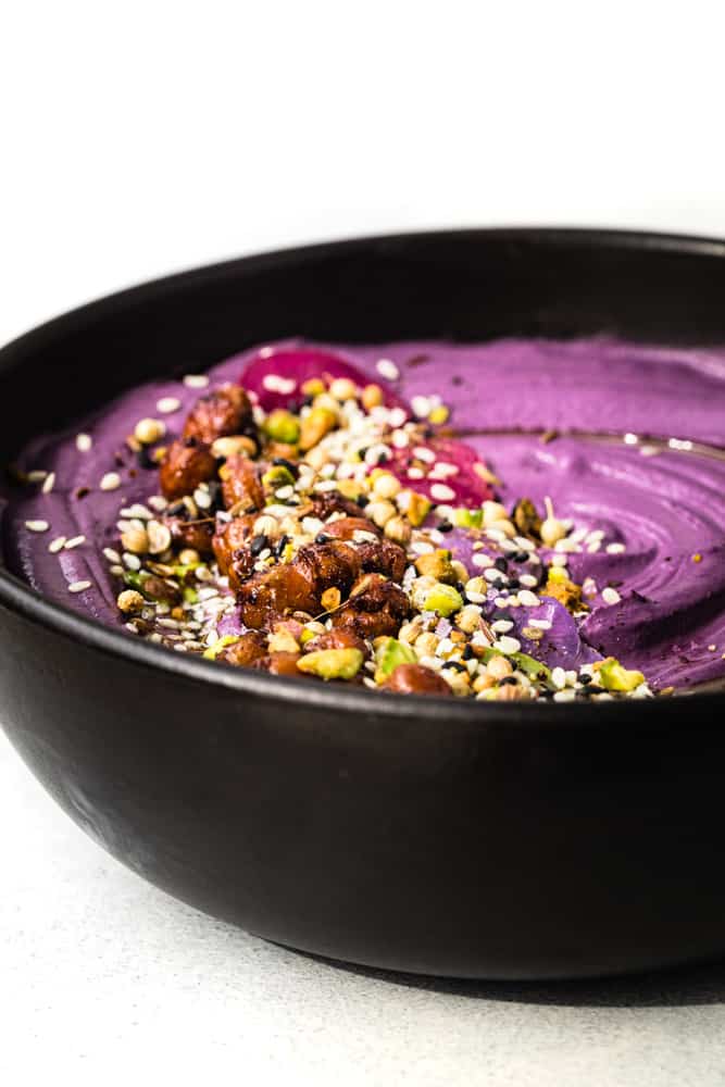 Side angle shot of purple carrot hummus in a black bowl with colorful toppings