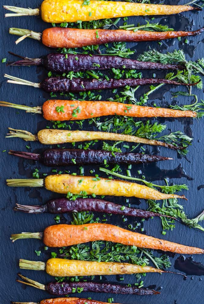 Roasted rainbow carrots topped with fresh herbs on a dark background; overhead shot