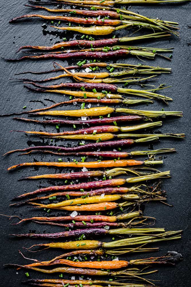 Roasted rainbow carrots topped with chives and flaky salt; overhead shot on a black background