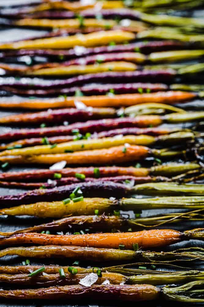 Roasted rainbow carrots, side-angle shot, topped with chives and flaky sea salt.