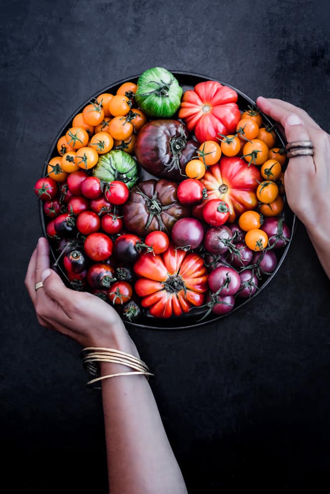 Daniela Gerson holding a black plate filled with different varieties of tomato that together create a rainbow!