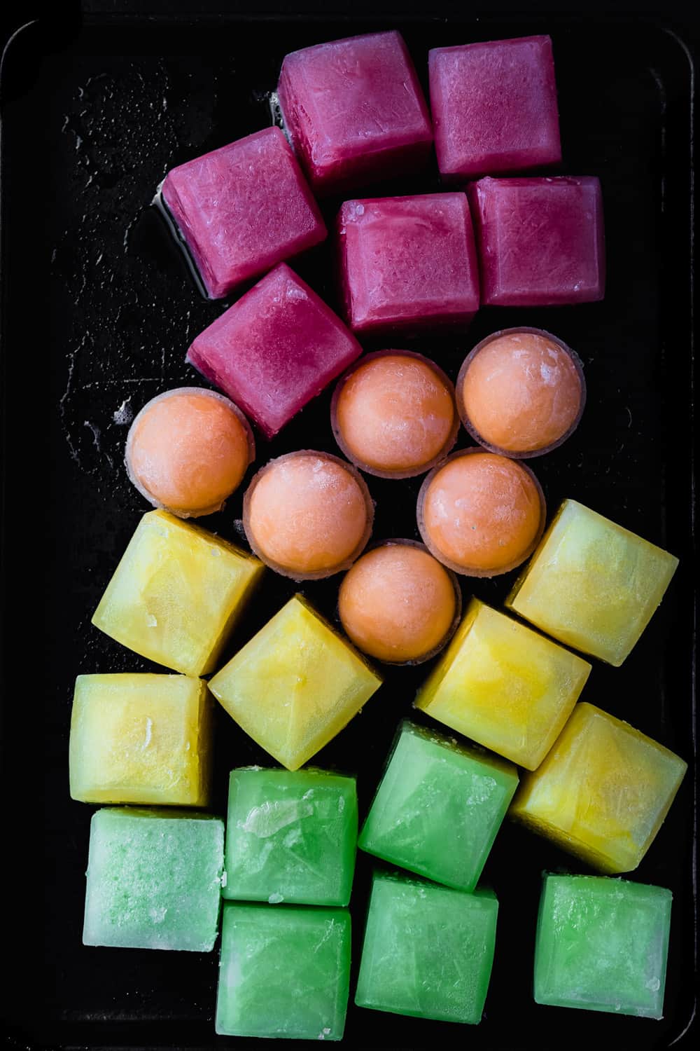 Red, orange, yellow and green melon ice; overhead shot on a black background