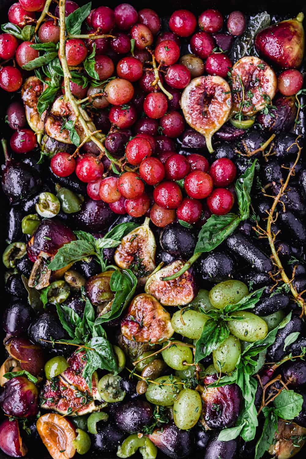 Balsamic & thyme roast grapes on a baking sheet with figs, olives and basil; pre-oven and over-head shot