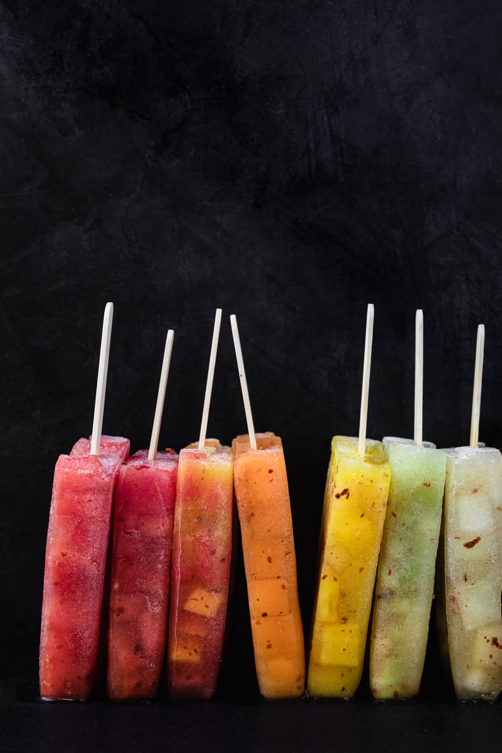 Colorful melon popsicles on top of red, orange, yellow and green melon ice.