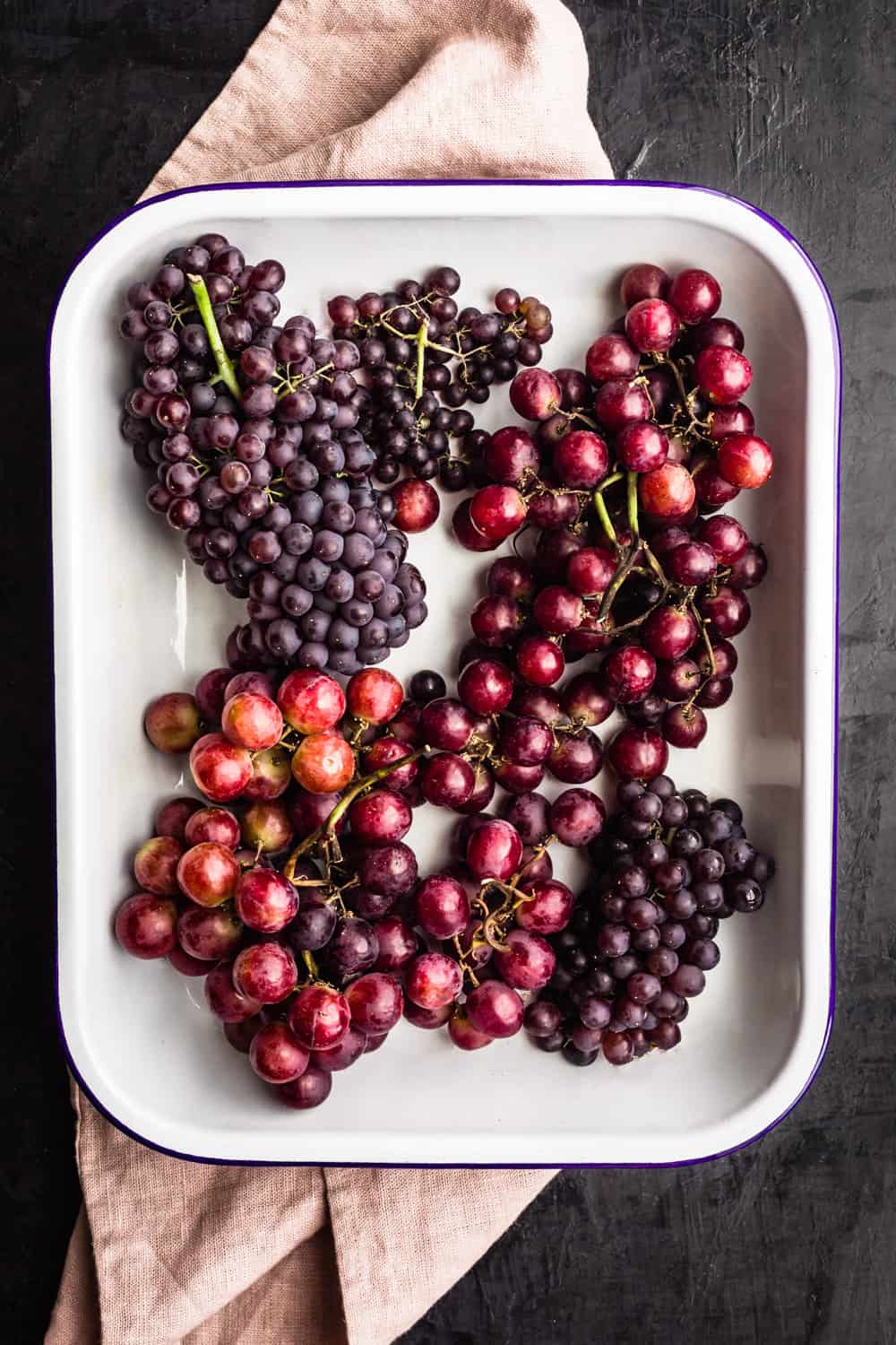 grapes in a sheet pan on top of a pink linen; overhead on a dark backdrop