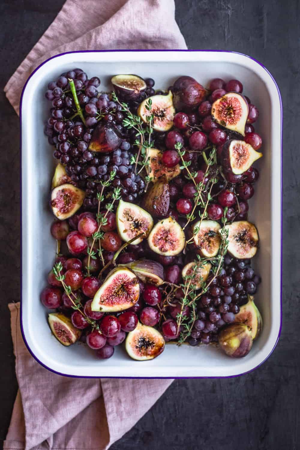 grapes and figs in a sheet pan with thyme; overhead shot on a dark backdrop