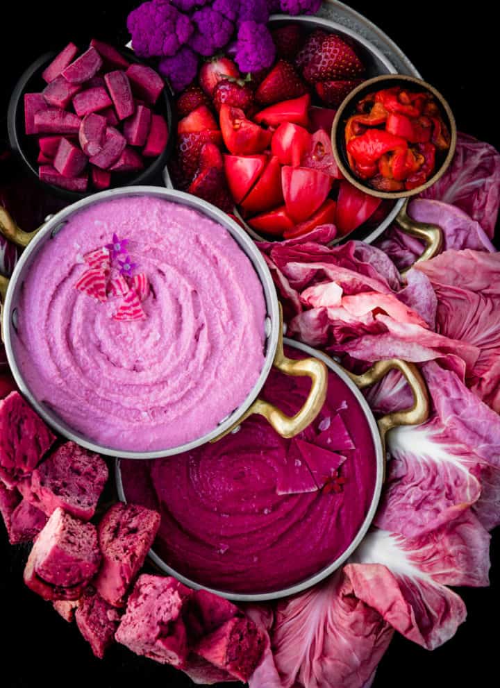 beet dips and pink foods on a cheese and appetizer board with pink fruits and veggies