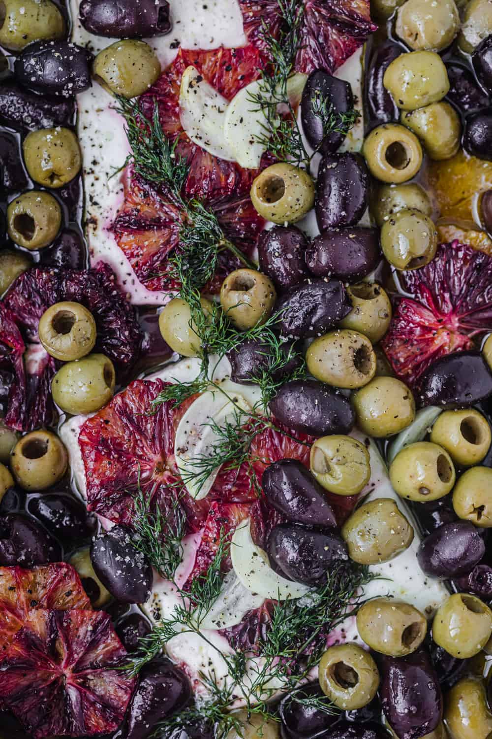 Baked feta dish - winter version topped with olives, blood orange and dill; overhead shot.