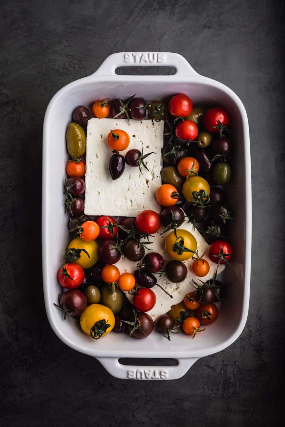 Feta in a baking dish with cherry tomatoes.