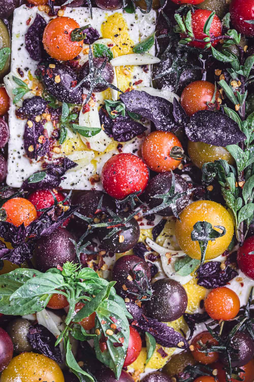 Feta topped with colorful cherry tomatoes, garlic, lemon and fresh herbs; overhead shot.