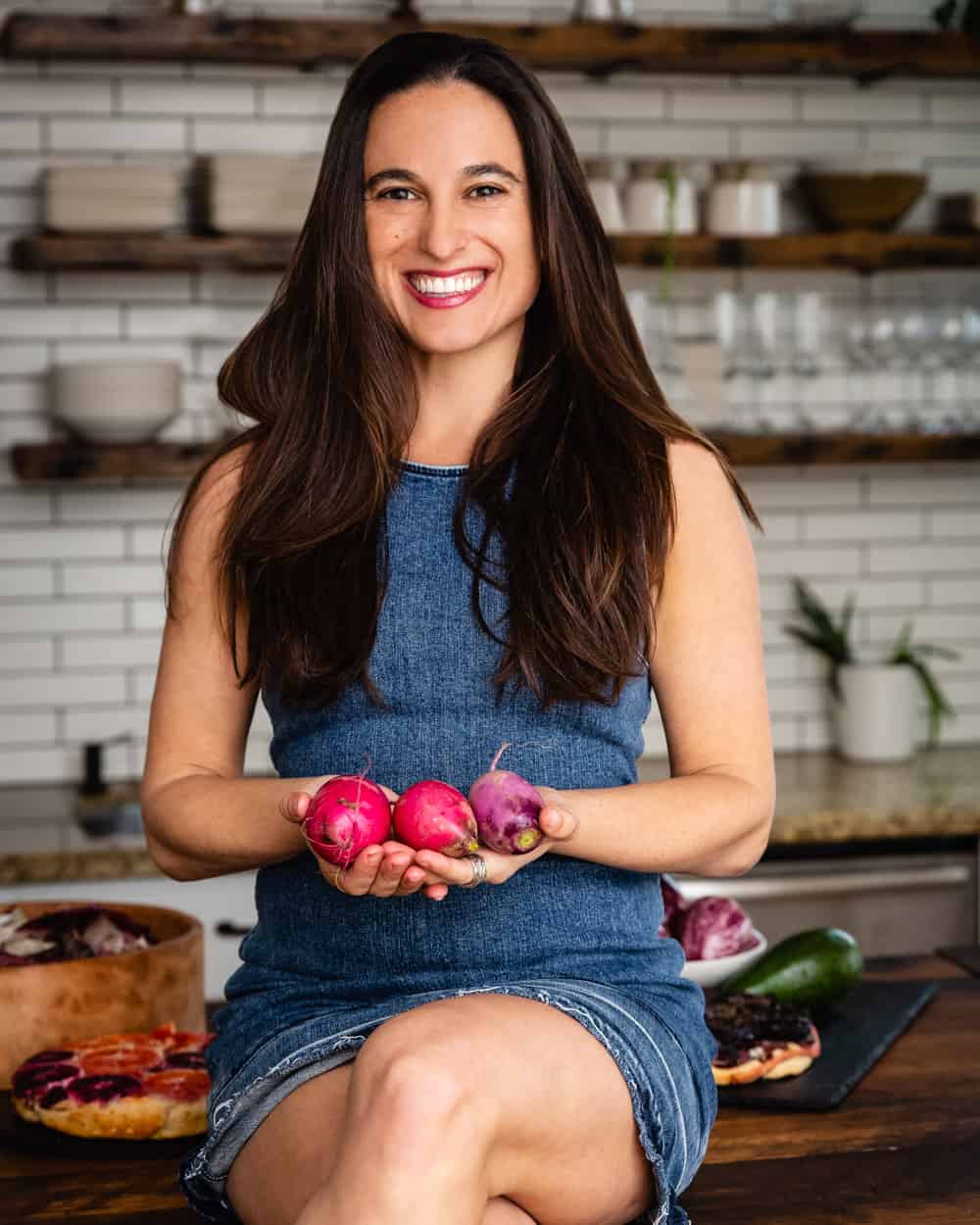 Los Angeles based food photographer Daniela Gerson sitting in the kitchen holding colorful veggies. 