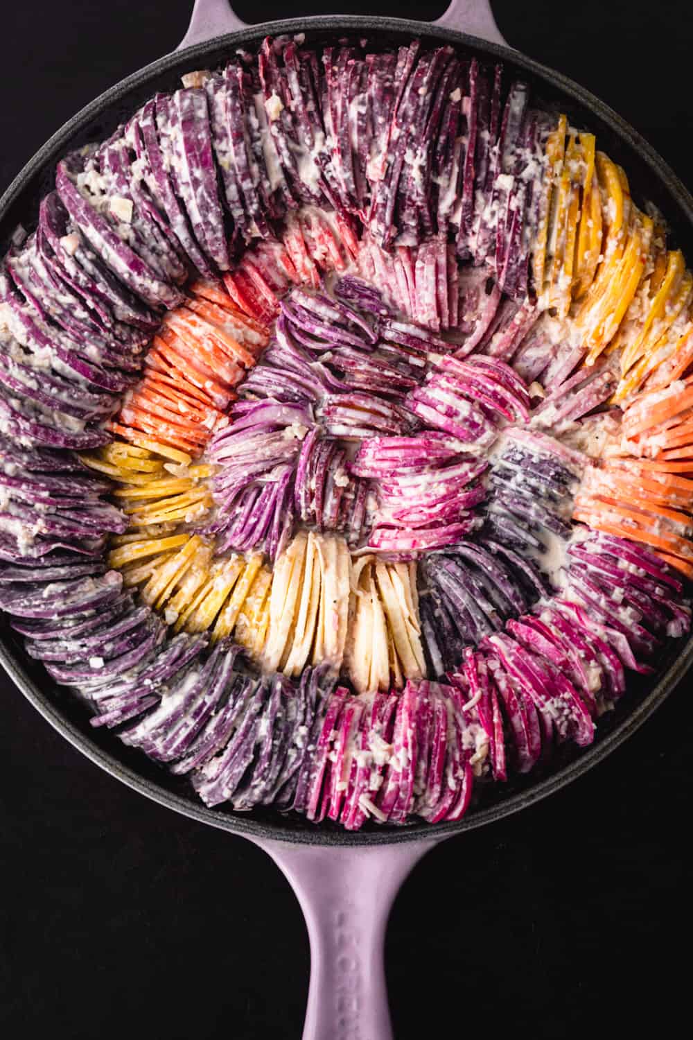 Rainbow root veggies including carrots, beets, potatoes, sweet potatoes, radishes and parsnips made into a very colorful hasselback gratin; proven shot.