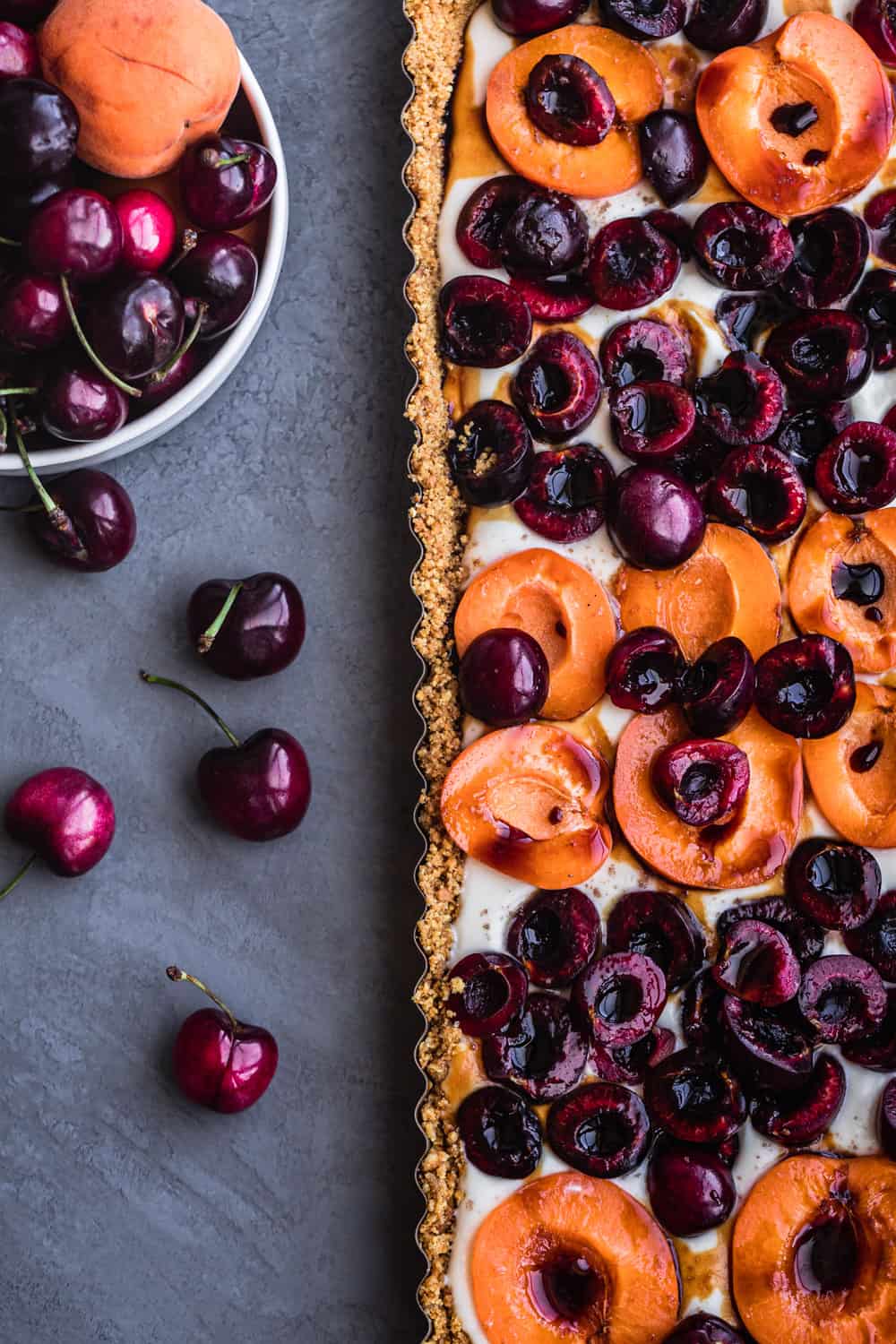 No bake cheesecake topped with fresh apricots and cherries, overhead shot on a grey background.