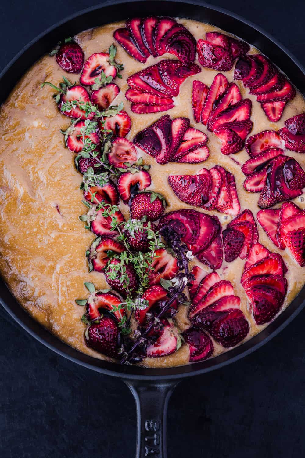 pre-oven olive oil cake topped with fresh strawberries; overhead shot on a black background