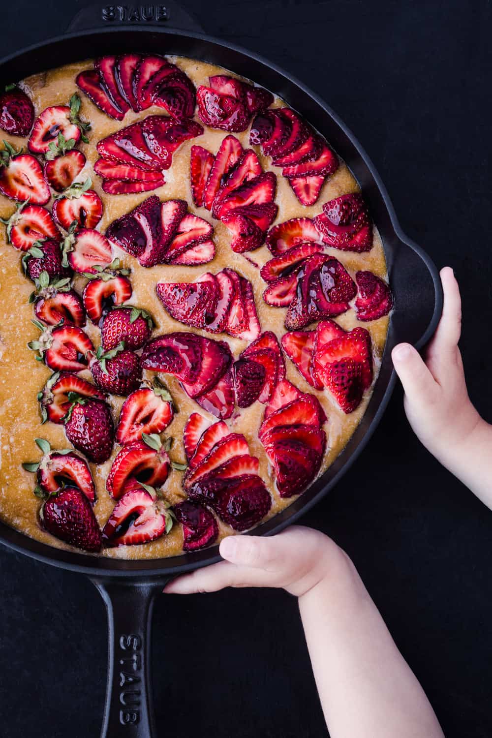 olive oil cake with strawberries in a cast iron skillet. pre-oven, with little kid hands on the skillet.