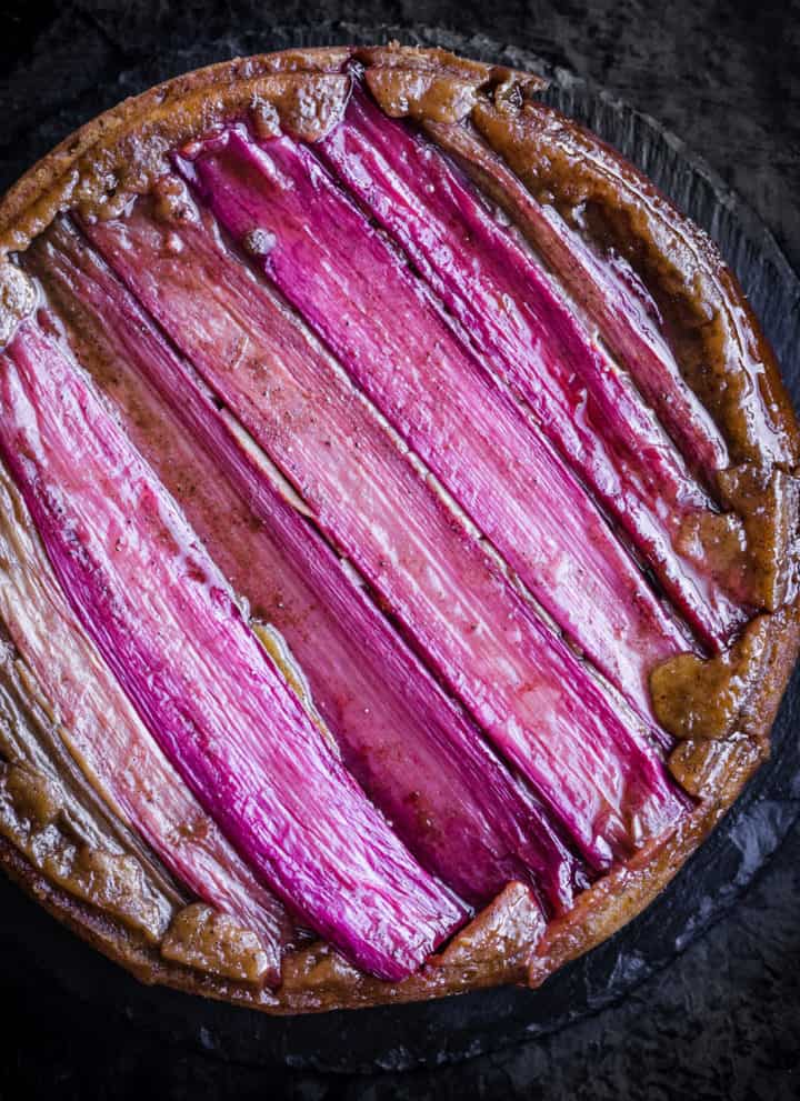 Finished rhubarb upside down cake, in cake pan on a black background; overhead shot.