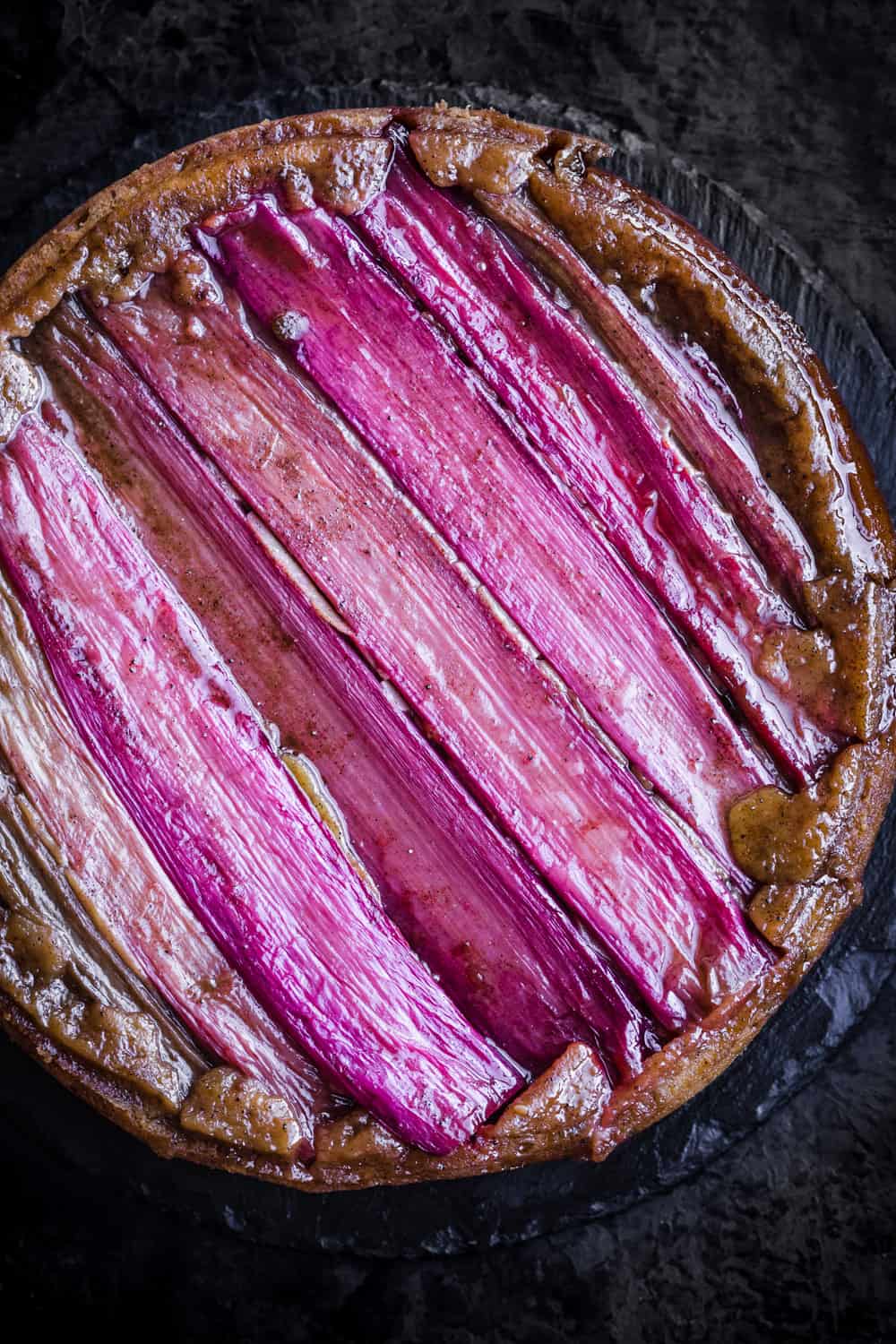 Finished rhubarb upside down cake, in cake pan on a black background; overhead shot.