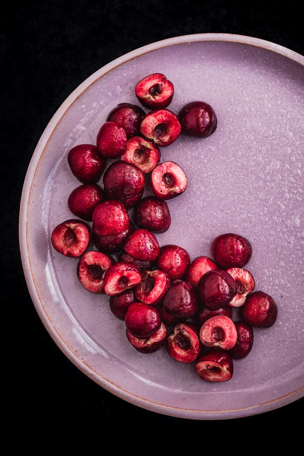 Pitting cherries, cut in half, on a pink plate, overhead shot.
