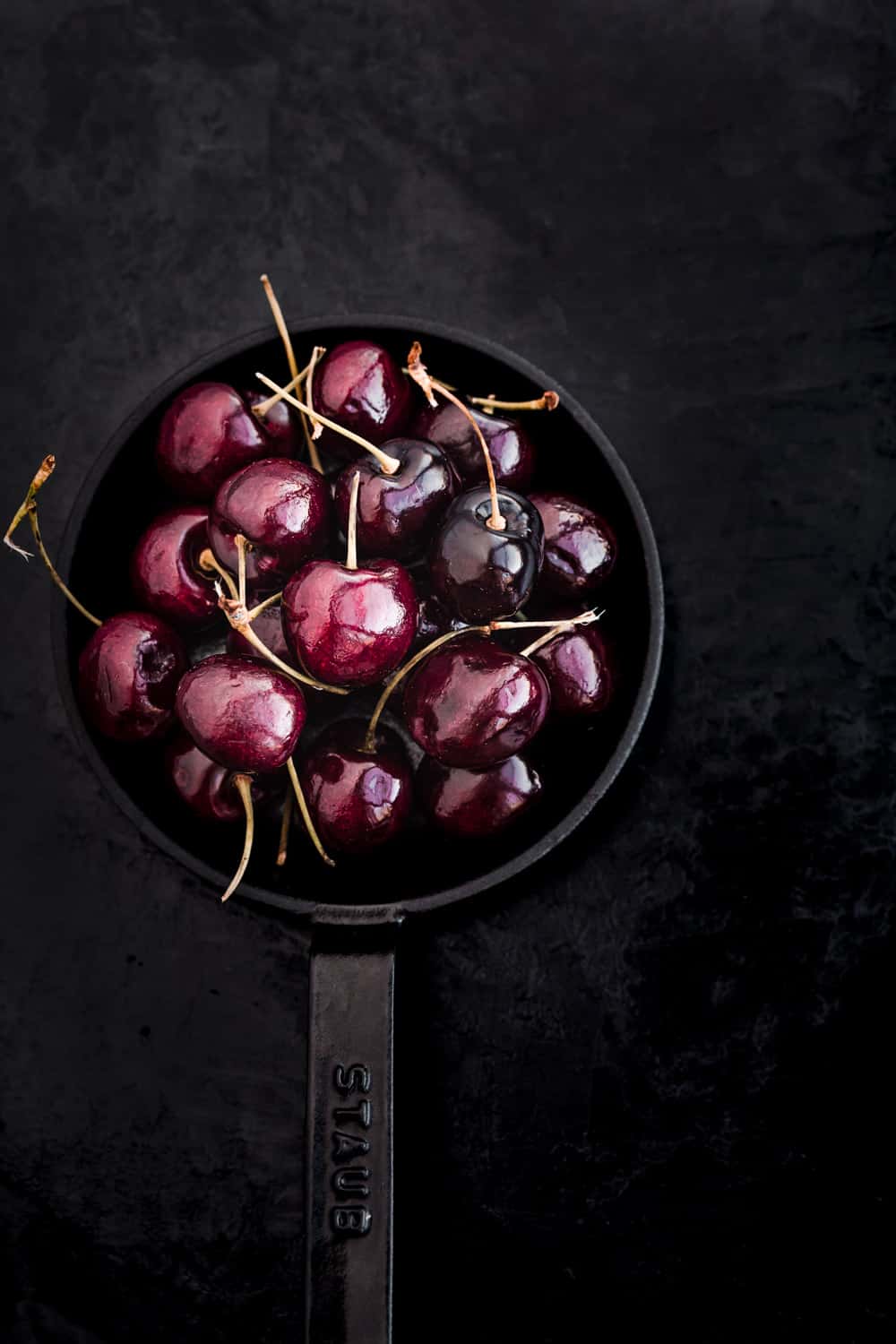 Whole cherries, with their stems, on a little cast iron skillet.