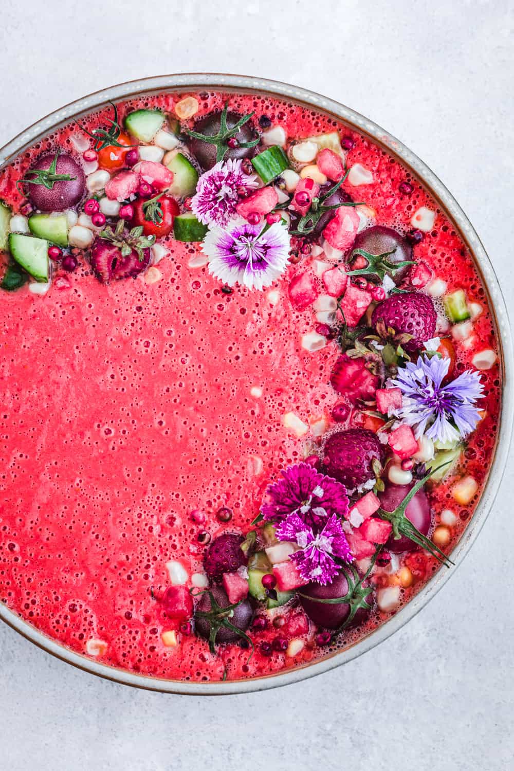 Pink gazpacho in a bowl, overhead shot on a white background.