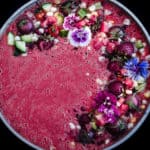 Over head shot of watermelon gazpacho with corn, cucumbers, strawberries, tomatoes, and edible flowers for topping.