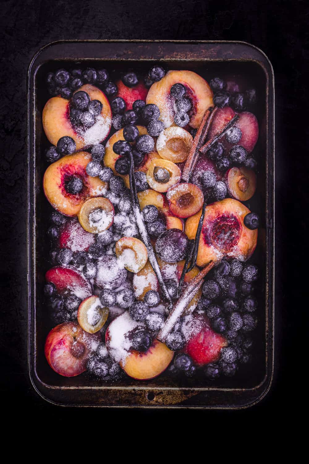 Peaches and other stone fruit in baking tray, sprinkled with sugar and other ingredients; ready to be baked.