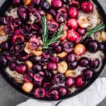 Raw chicken thighs topped with cherries and rosemary in a skillet; overhead shot.
