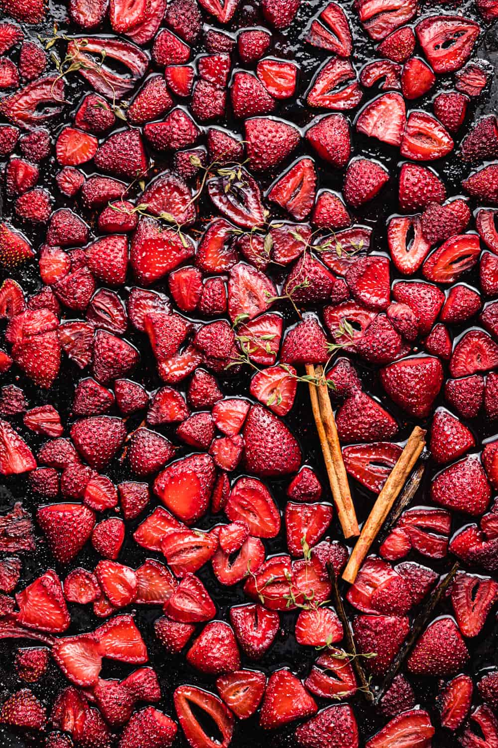 roasted strawberries with cinnamon sticks, vanilla beans and thyme on a baking sheet.
