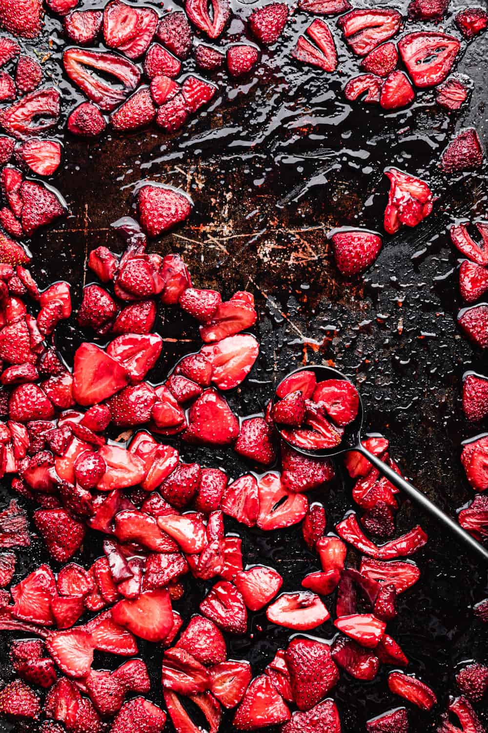 roasted strawberries on a baking sheet with a black spoon