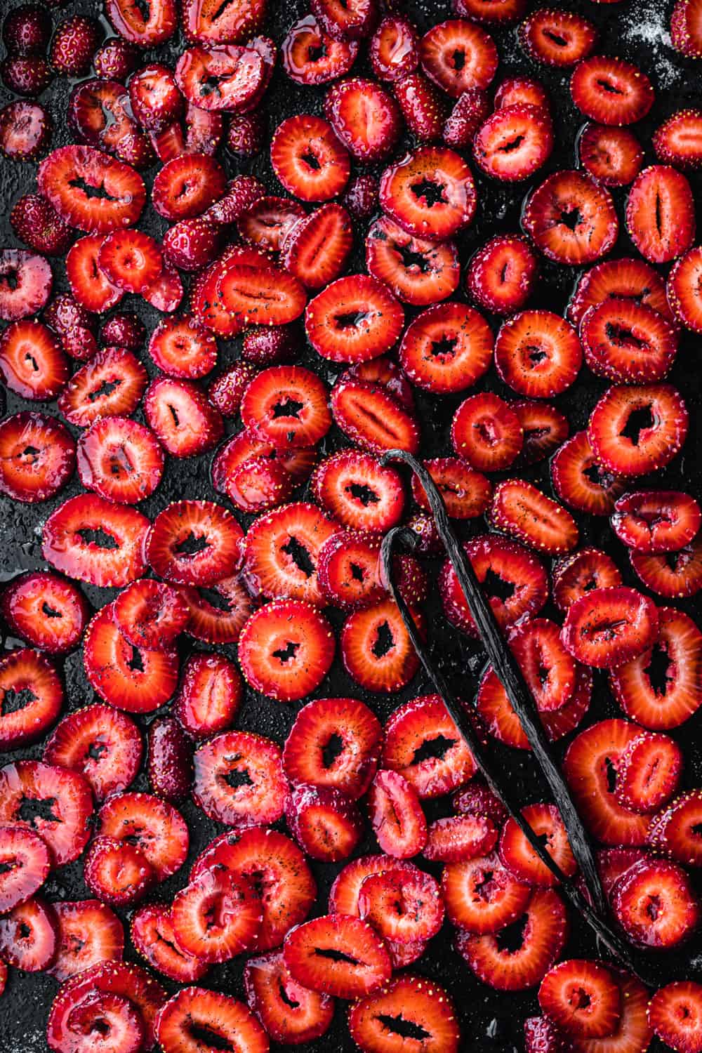 sliced strawberries with sugar, salt and vanilla beans on a baking sheet