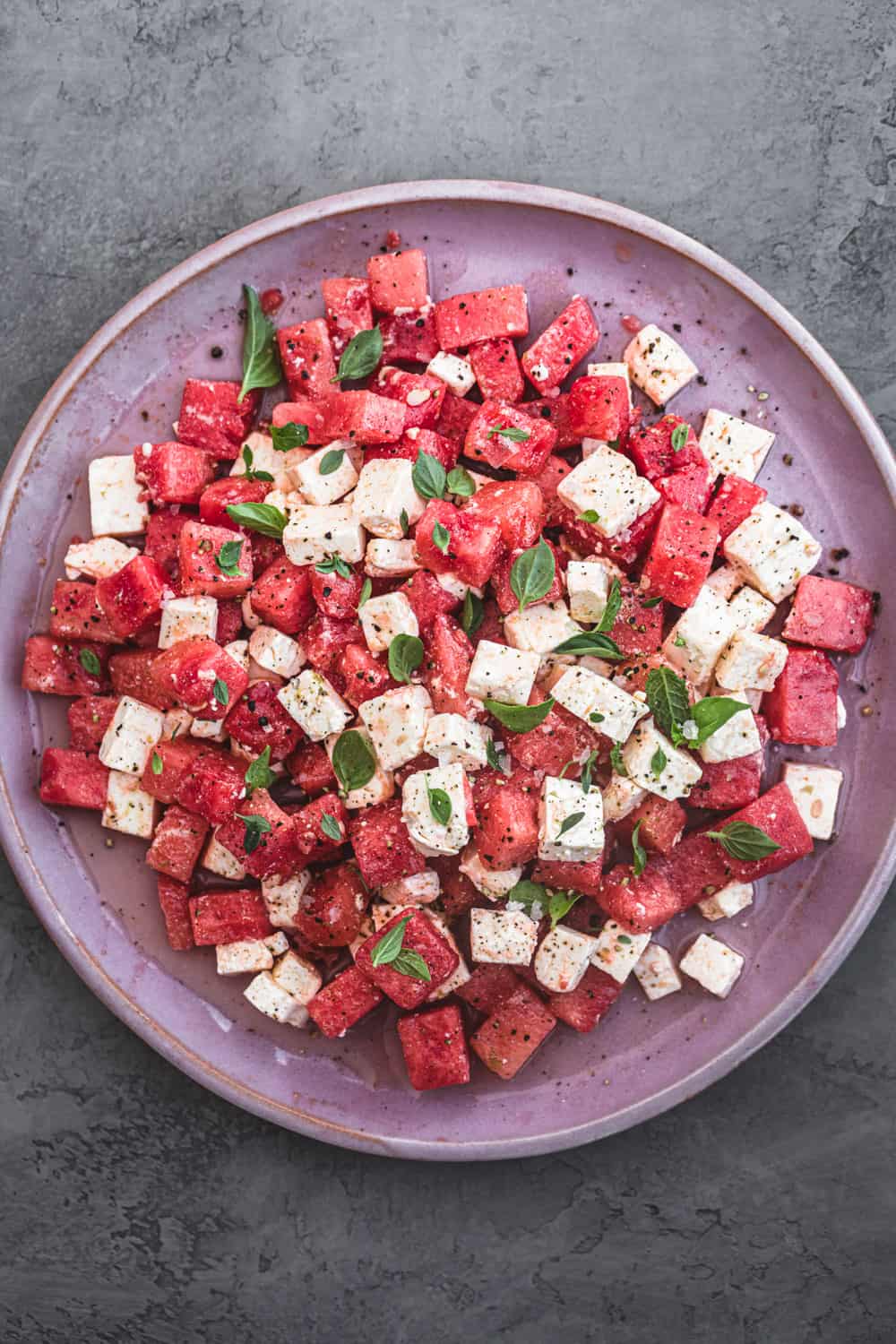 Watermelon feta salad with fresh herbs. Overhead shot on a pink plate.
