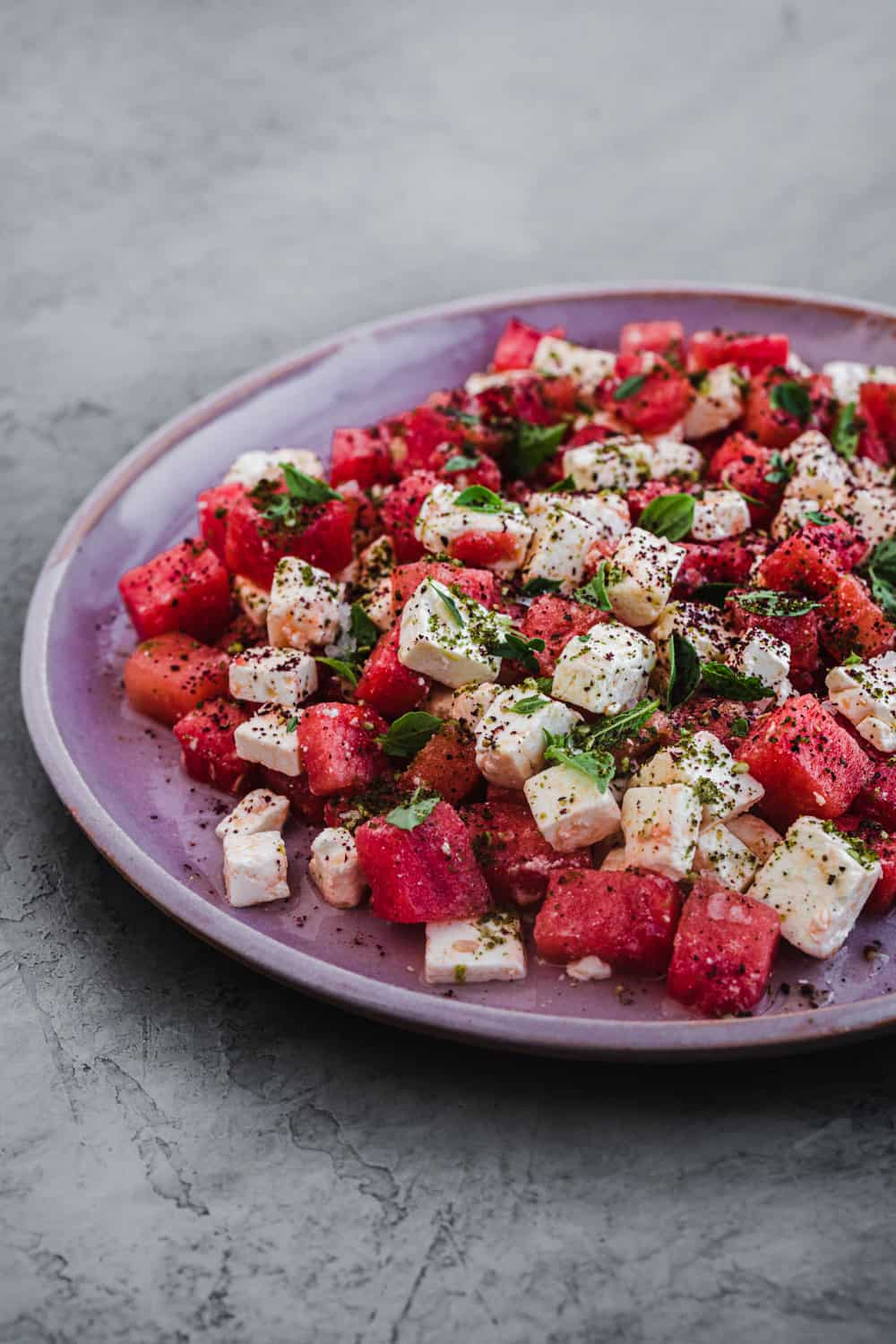 Watermelon Feta Salad topped with fresh herbs and spices. Side angle shot.