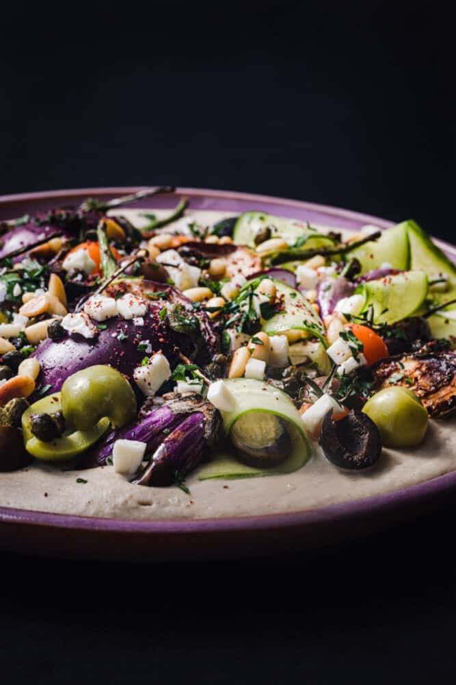 Side angle and close up loaded hummus topped with colorful vegetables, herbs and spices.