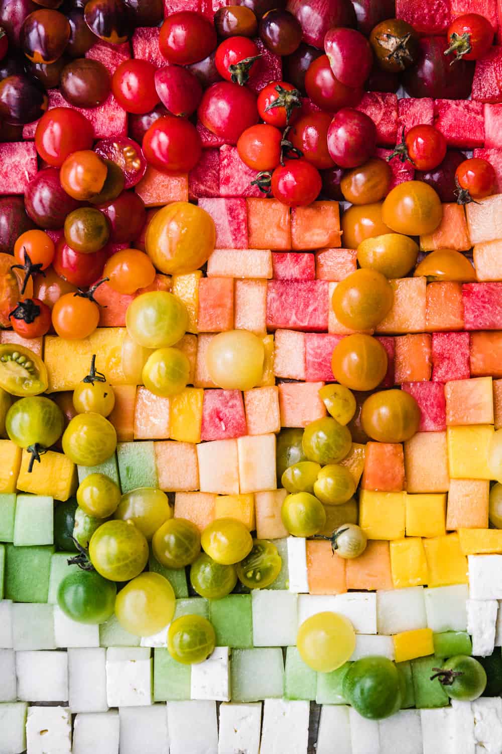 cubed melon, tomatoes, feta, mango and papaya arranged like a rainbow on a tray; overhead.