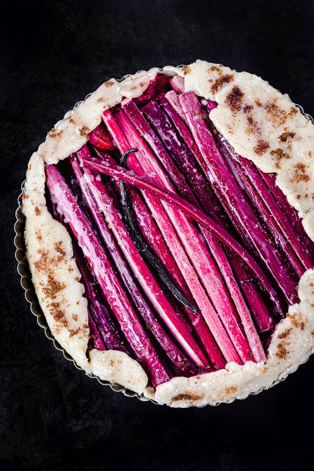 Assembled rhubarb galette pre-oven, overhead shot on a black background.