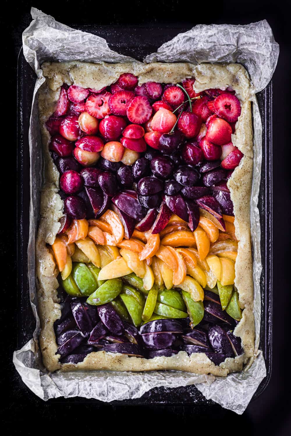 Pre-oven colorful stone fruit galette in a pan; overhead on a black background.