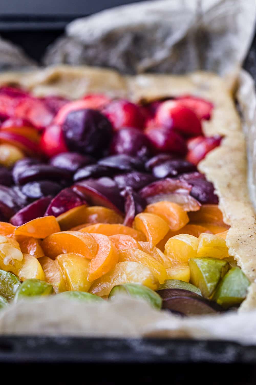 side angle and up close stone fruit galette with green, yellow, orange, purple and red varieties of stone fruits.