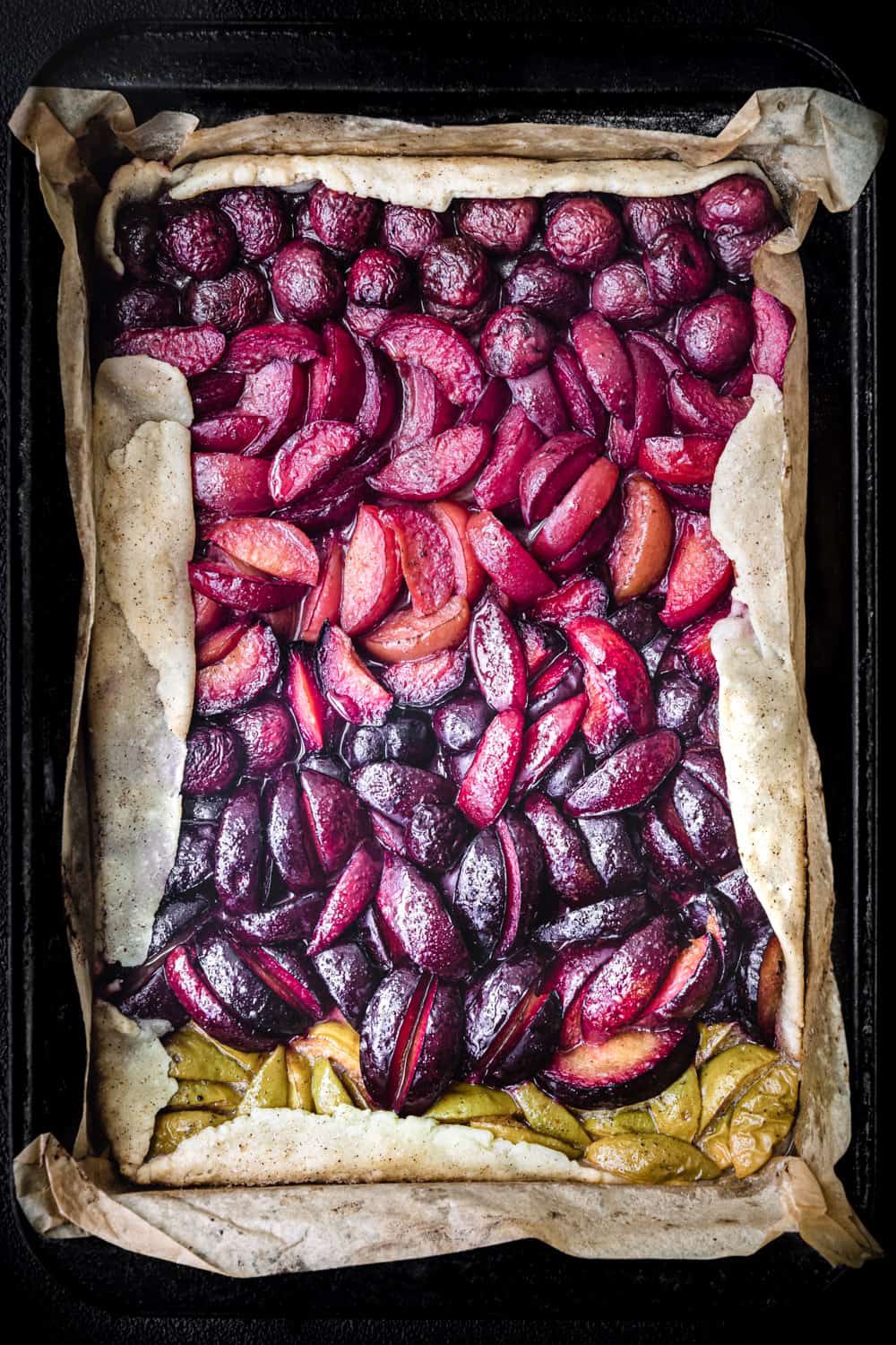 Cooked cherry and plum galette in pan with red, pink, purple and green fruits; overhead.