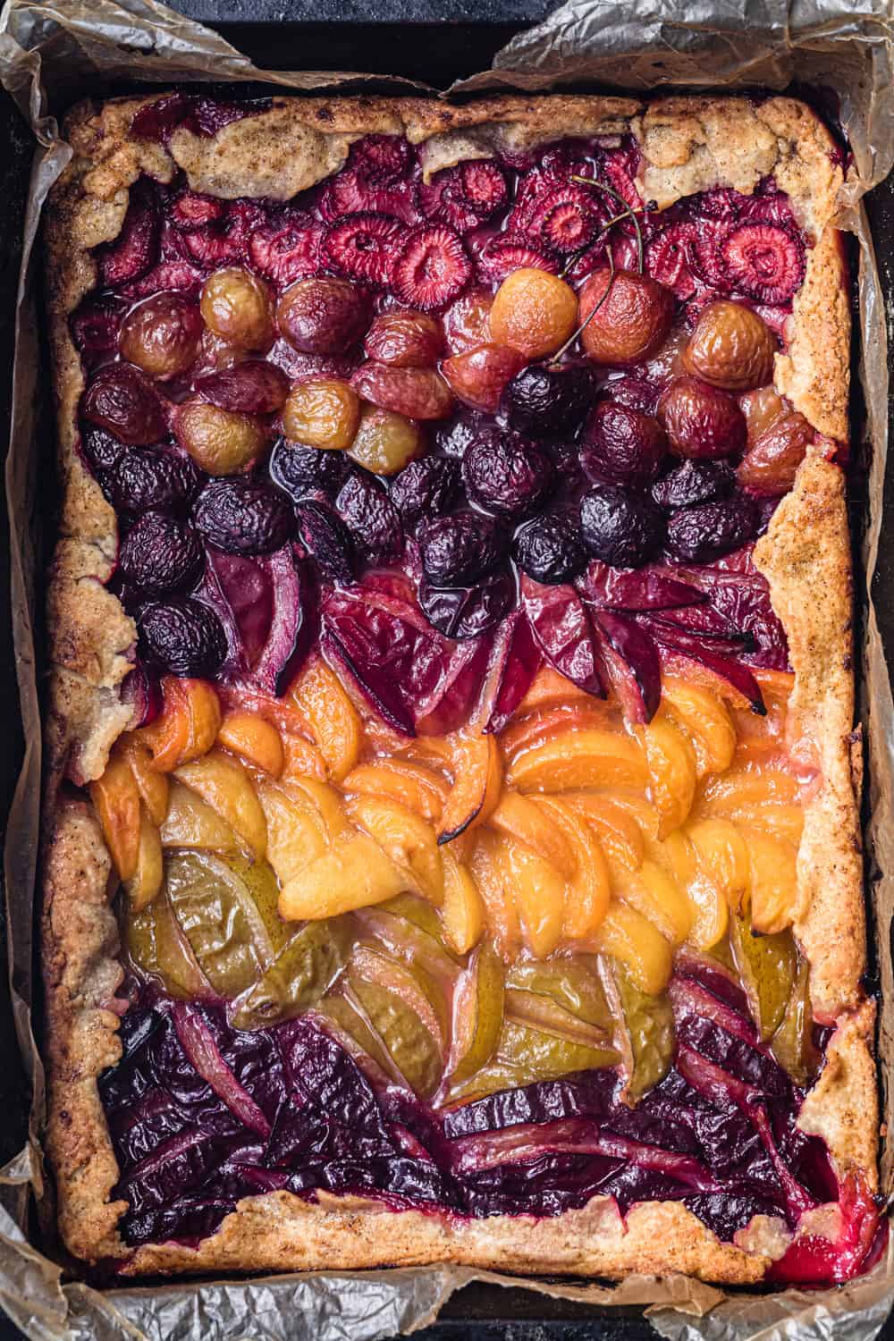 cooked stone fruit galette with strawberries, cherries, apricots, and plums in a pan; overhead