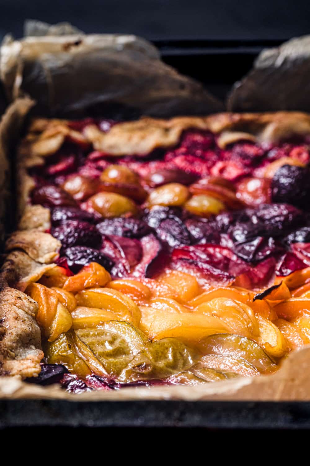 colorful stone fruit galette with plums, cherries, apricots, and strawberries; up close and side angle.