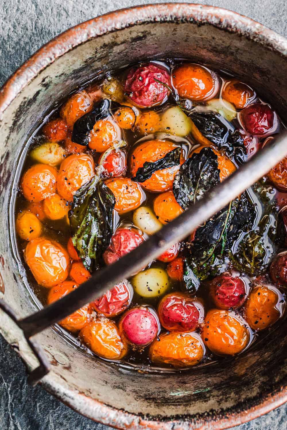 Tomato confit in a copper pot with garlic and basil; overhead shot.