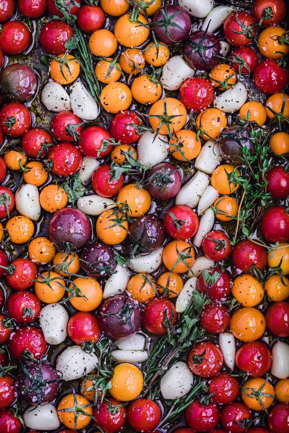 colorful cherry tomatoes with fresh herbs, garlic and olive oil in a baking dish and ready to be roasted