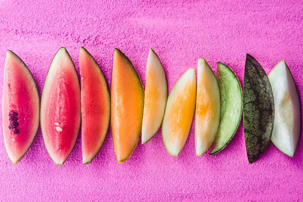 pink, orange, yellow, green and white melon slices on a pink background