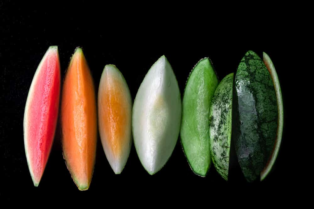 pink, orange, yellow, green and white melon slices on a black background