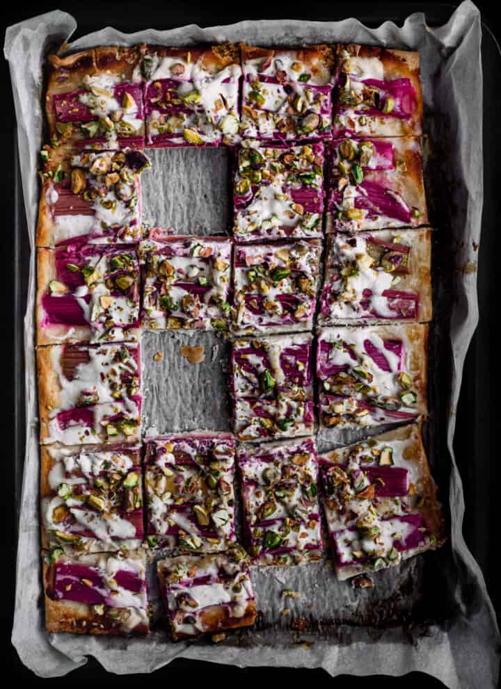 Rhubarb tart sprinkled with pistachios and drizzled with honey, cut into square, overhead and a few squares missing.