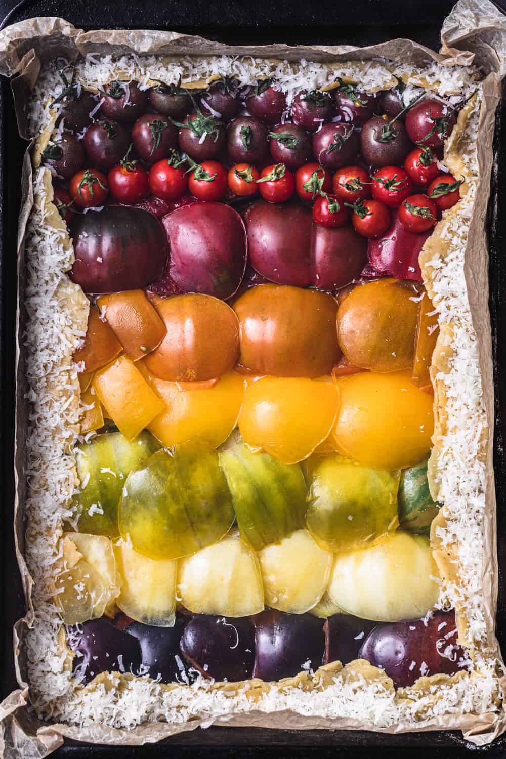 a raw tomato galette, with colorful red, orange, yellow, green and purple tomatoes arranged like a rainbow.