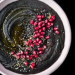 black hummus in a pink bowl with toppings, overhead shot