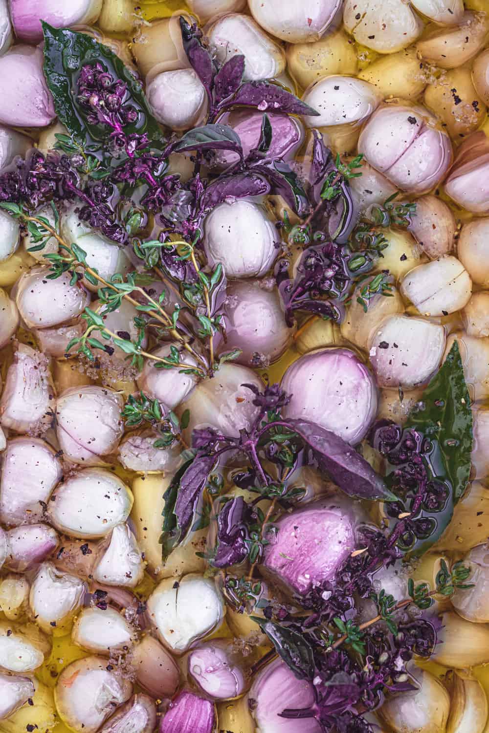 Raw shallots covered in oil oil and topped with basil in a baking dish.