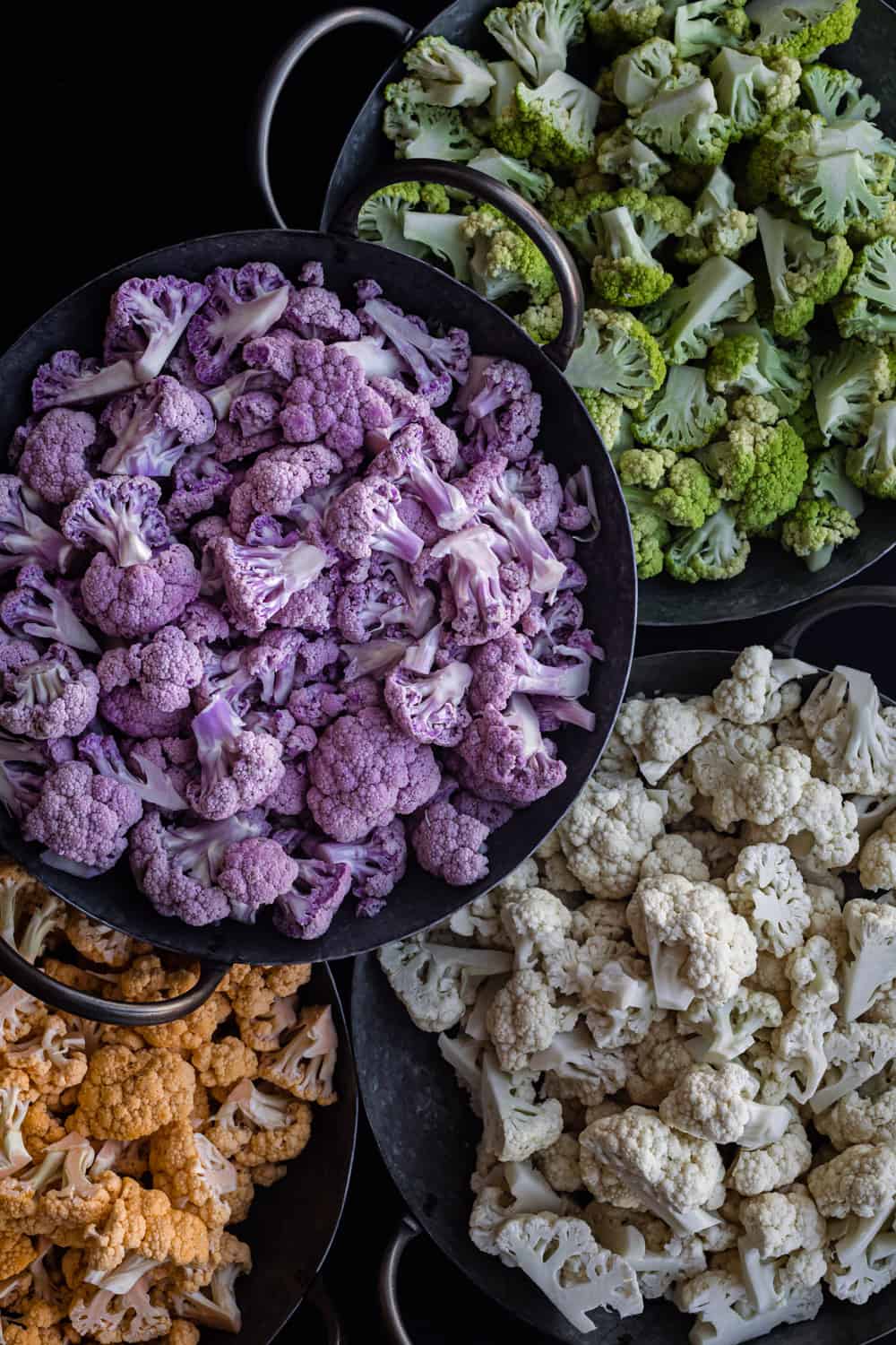 purple, green, orange and white cauliflower florets, separated by color, in silver bowls