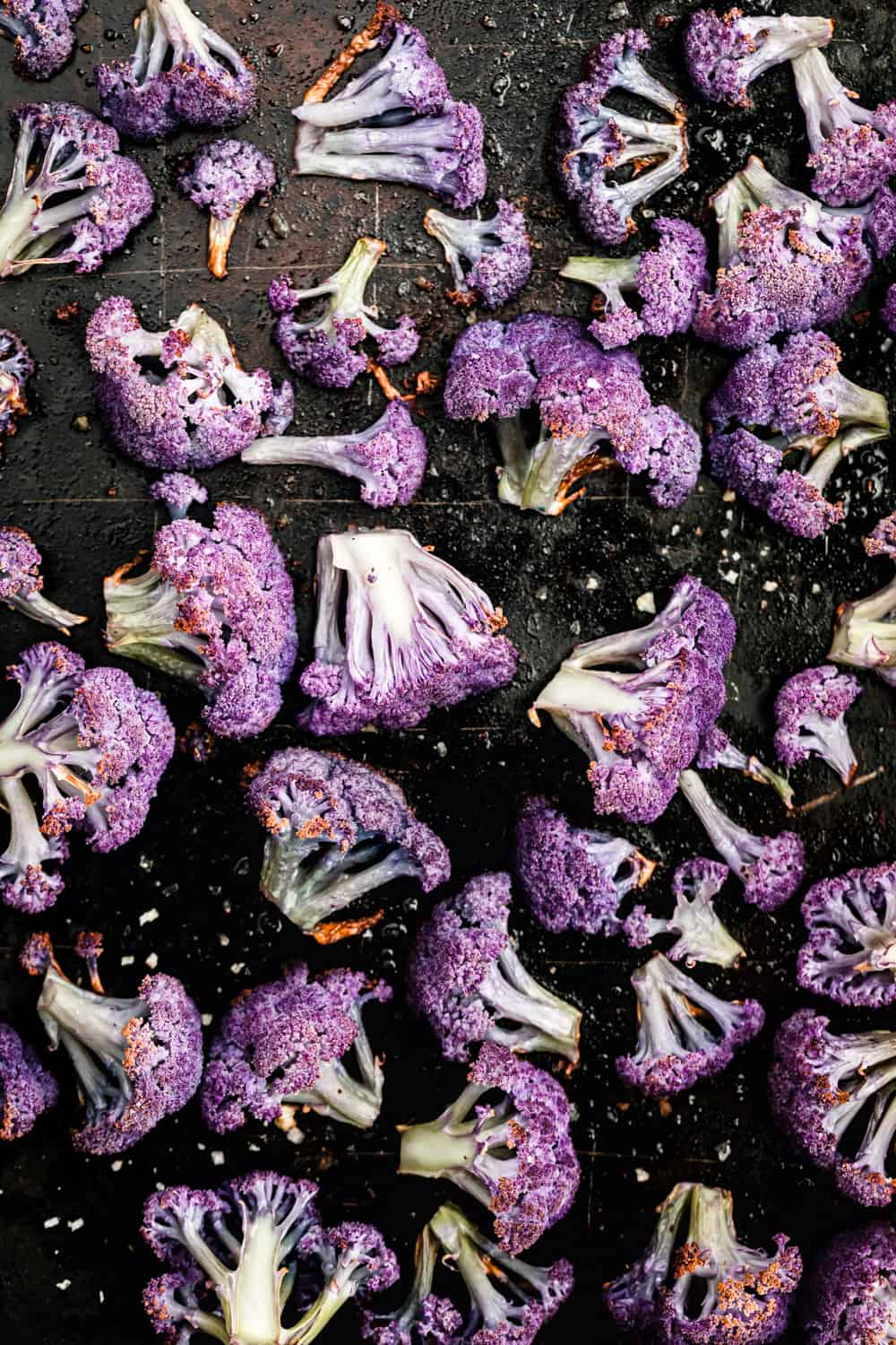 roasted purple cauliflower florets, on a black baking sheet, overhead